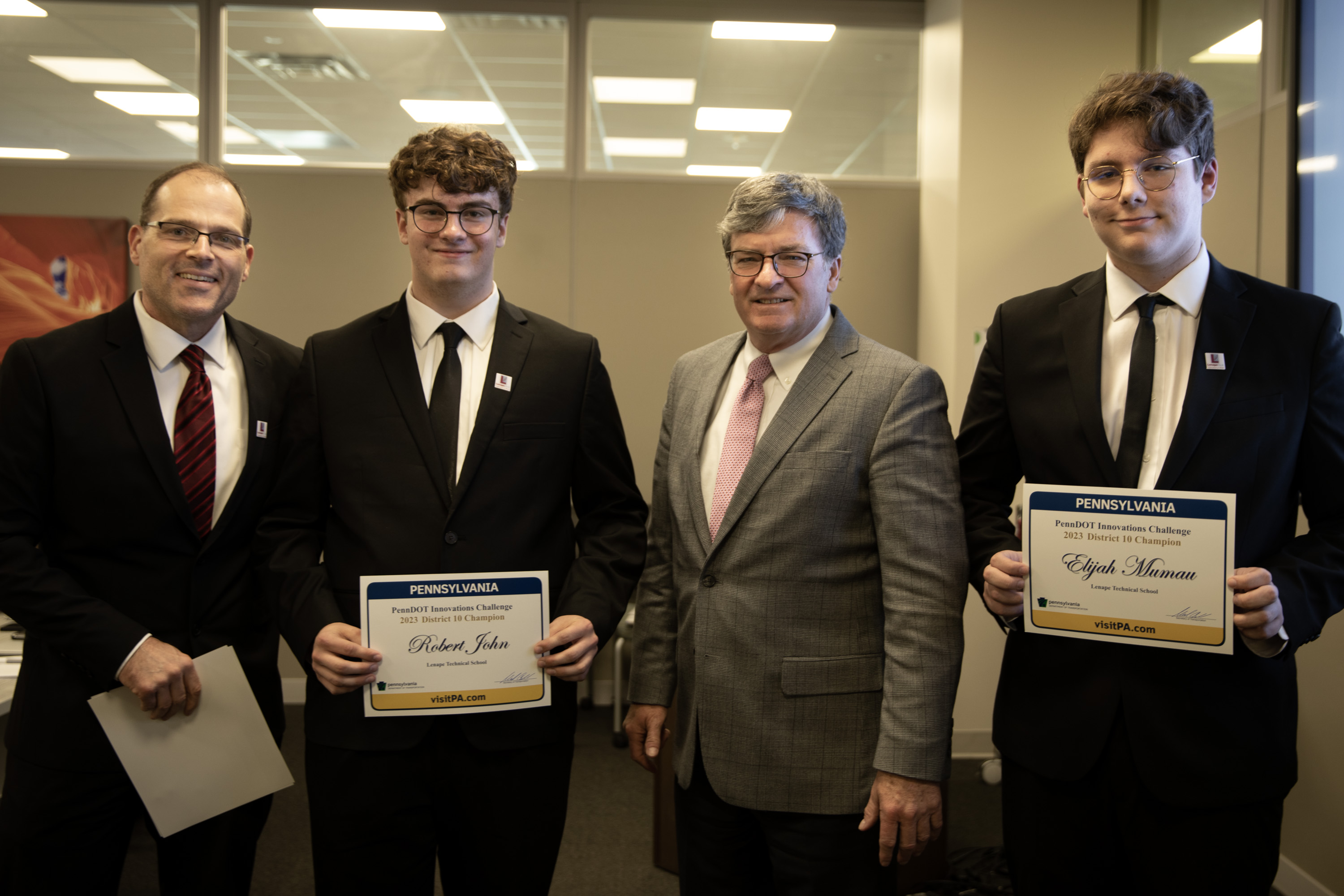An image of PennDOT Secretary Michael Carroll standing in a row along with Lenape Technical School advisor Jason Zimmerman and students Elijah Mumau and Robert John who are receiving their certificates for winning the regional competition and moving on to the statewide judging event